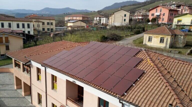 Un edificio con dei pannelli fotovoltaici rossi sopra, che si uniformano al colore del tetto.